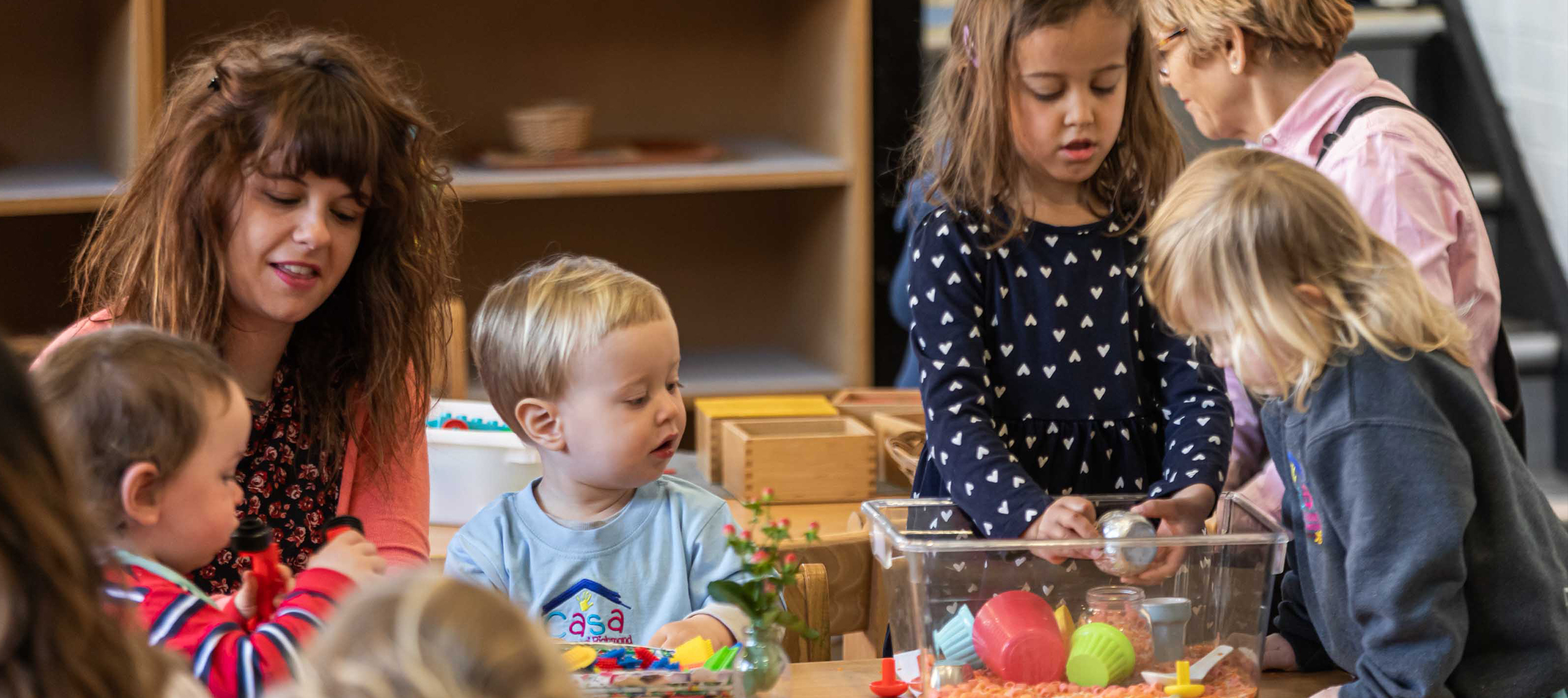 An educator and children exploring a sensory tray together at Casa Montessori Richmond