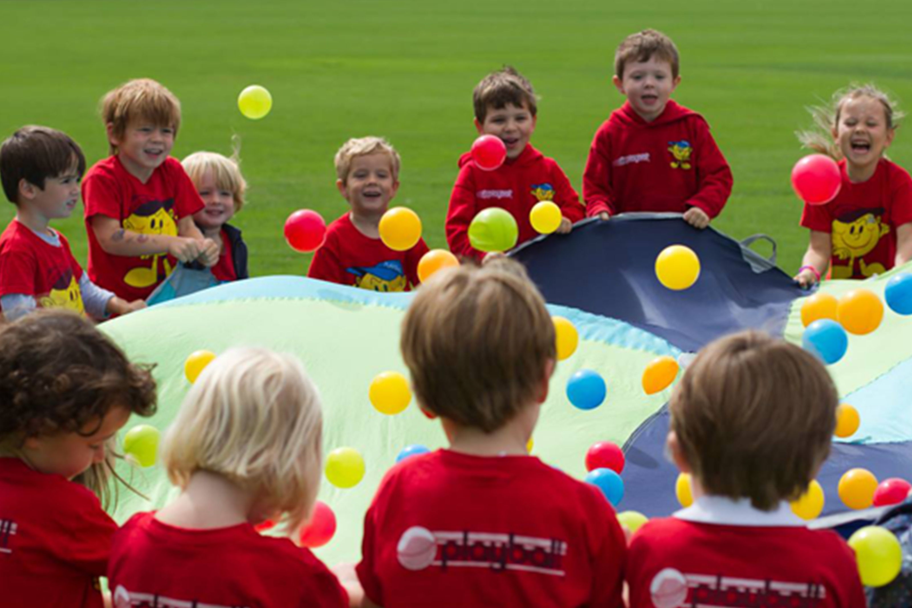 Children playing a parachute game with colourful balls at a Playball session